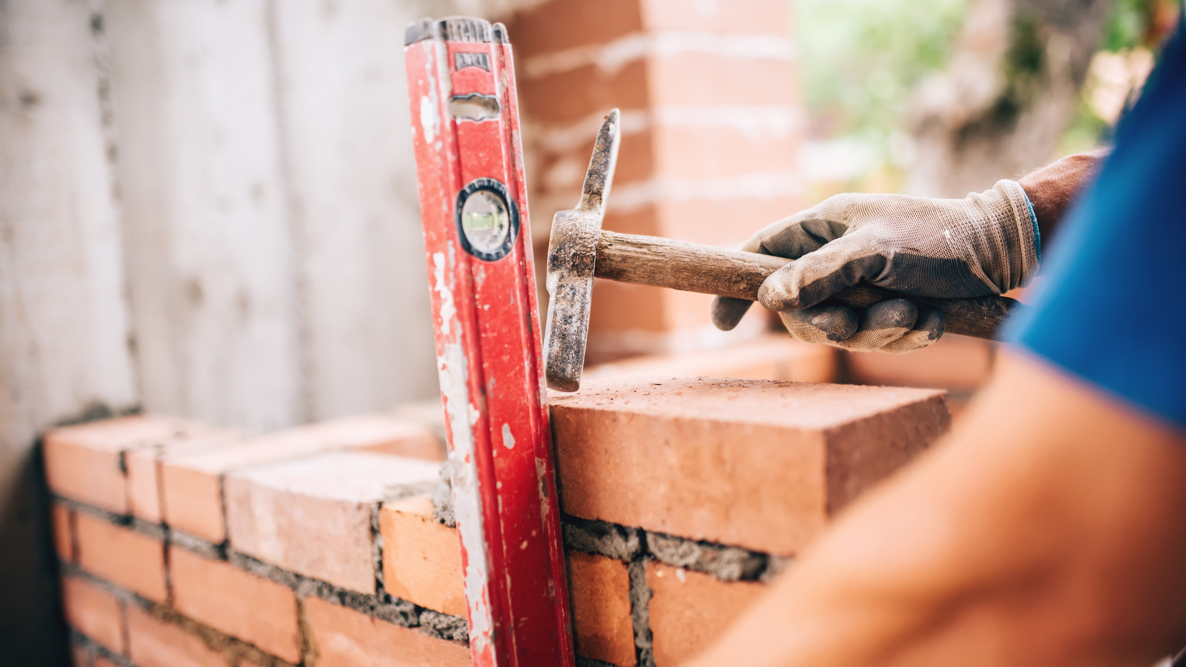 Bricklayer holding hammer near brick wall