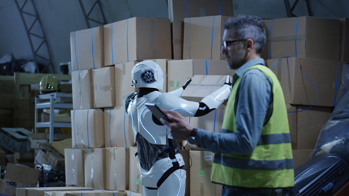 Man alongside robot picking up box inside warehouse