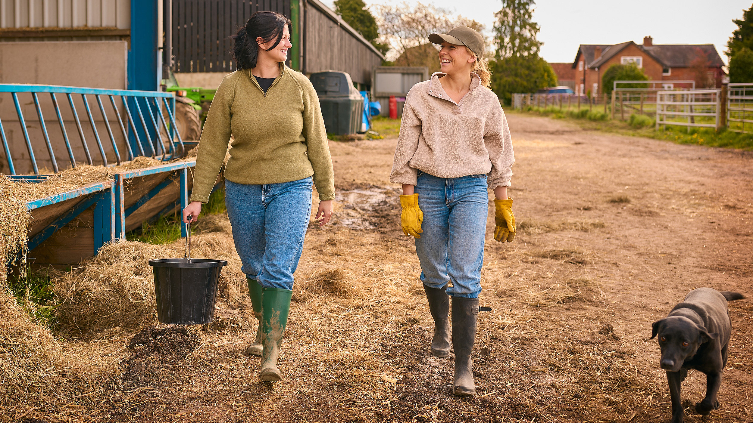 Women farmers walking through farmyard with labrador