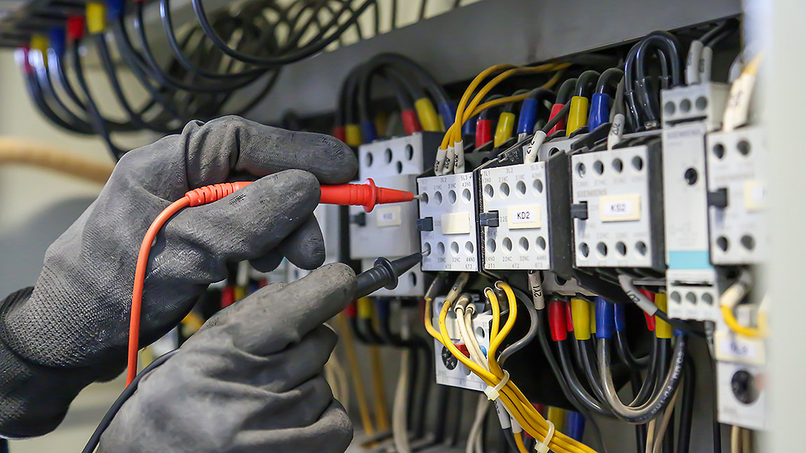 Electrical engineer using digital multi-meter measuring equipment to checking electric current voltage at circuit breaker and cable wiring system in main power distribution board