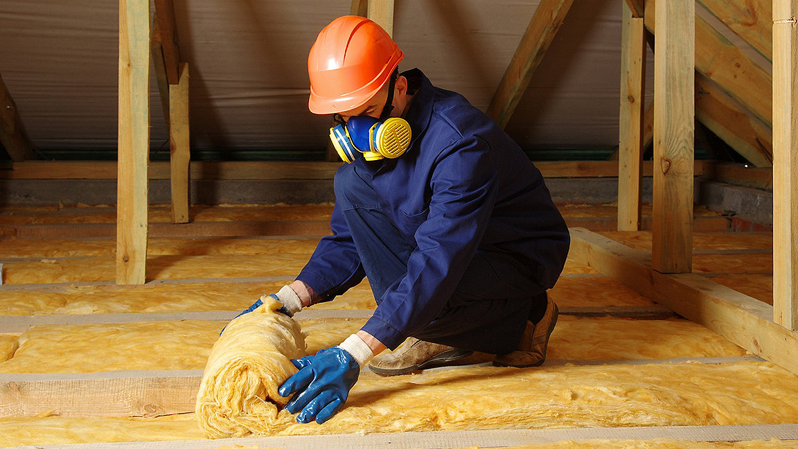 Photo of construction worker thermally insulating house attic with glass wool