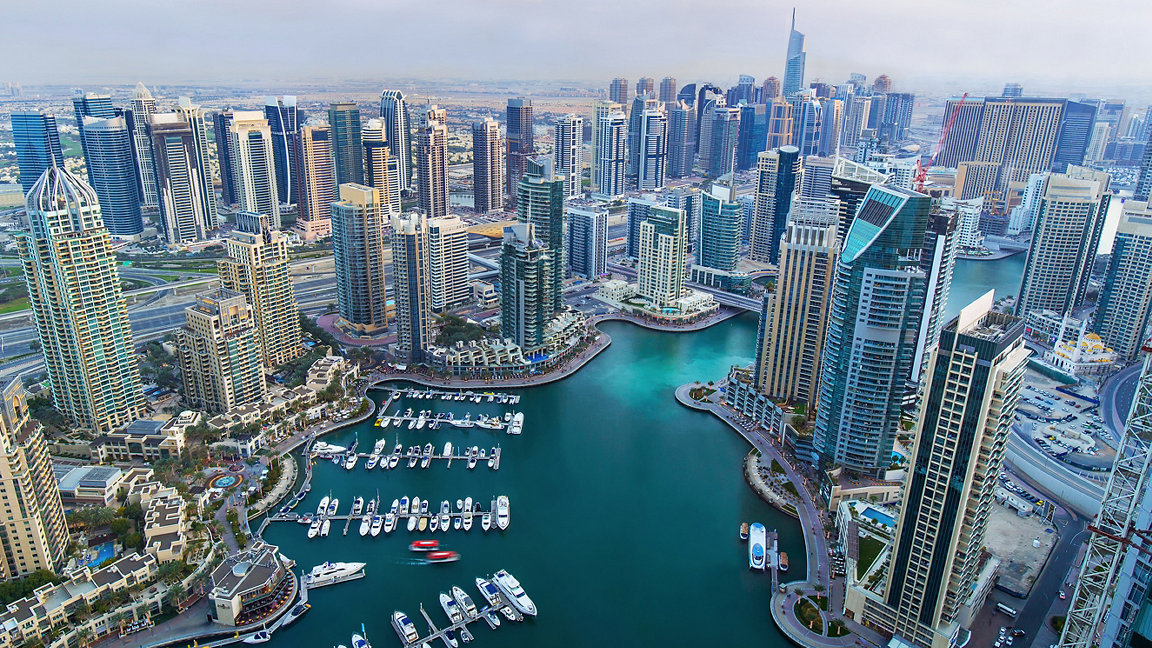Dubai Marina - aerial view of skyscrapers around water with moored boats at bottom of the image