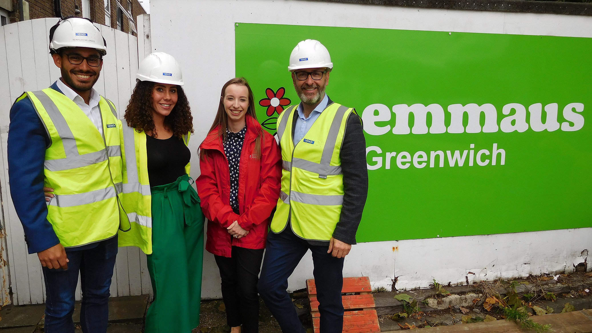 Four construction professionals stand in front of emmaus Greenwich banner