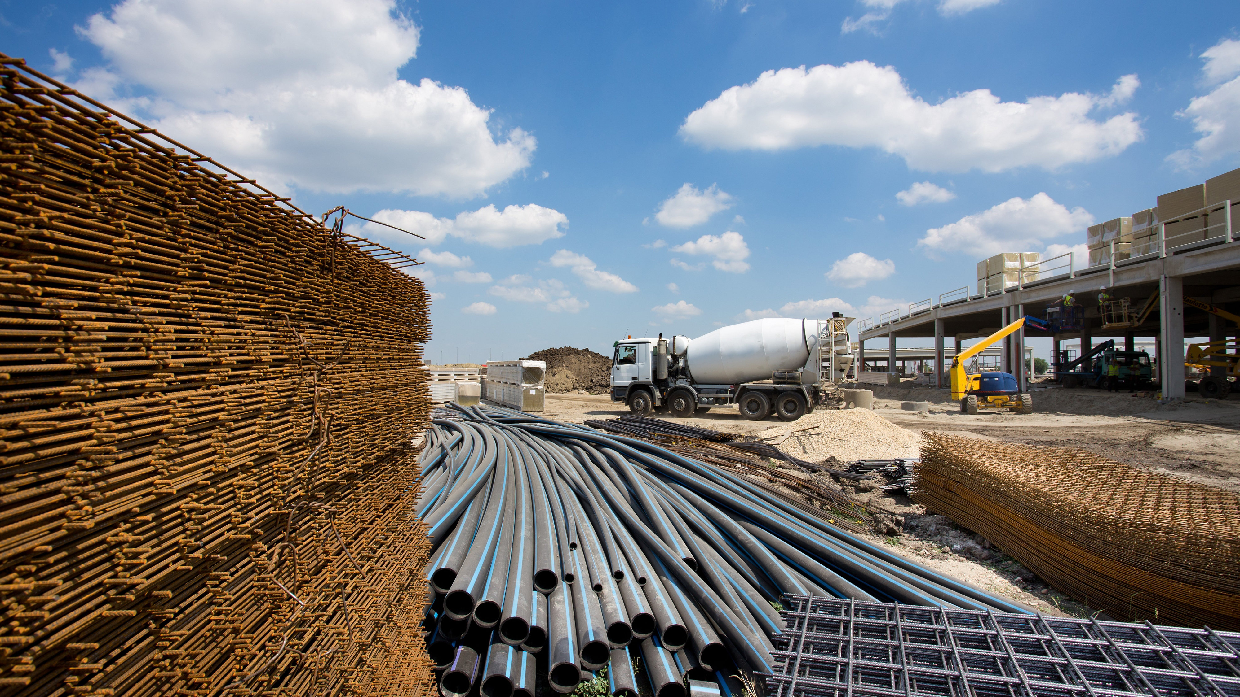 construction materials - wood, steel, pipes - on site. cement mixer and digger in background.