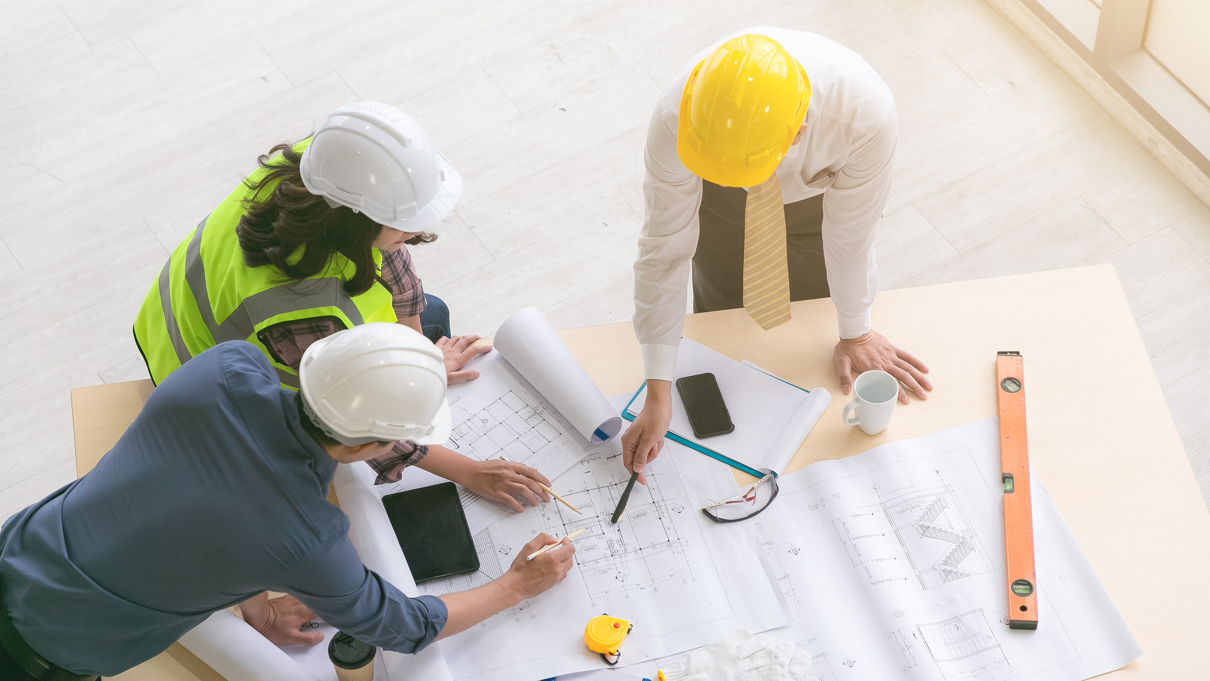 Three professionals leaning over a building plan discussing the contents of the document