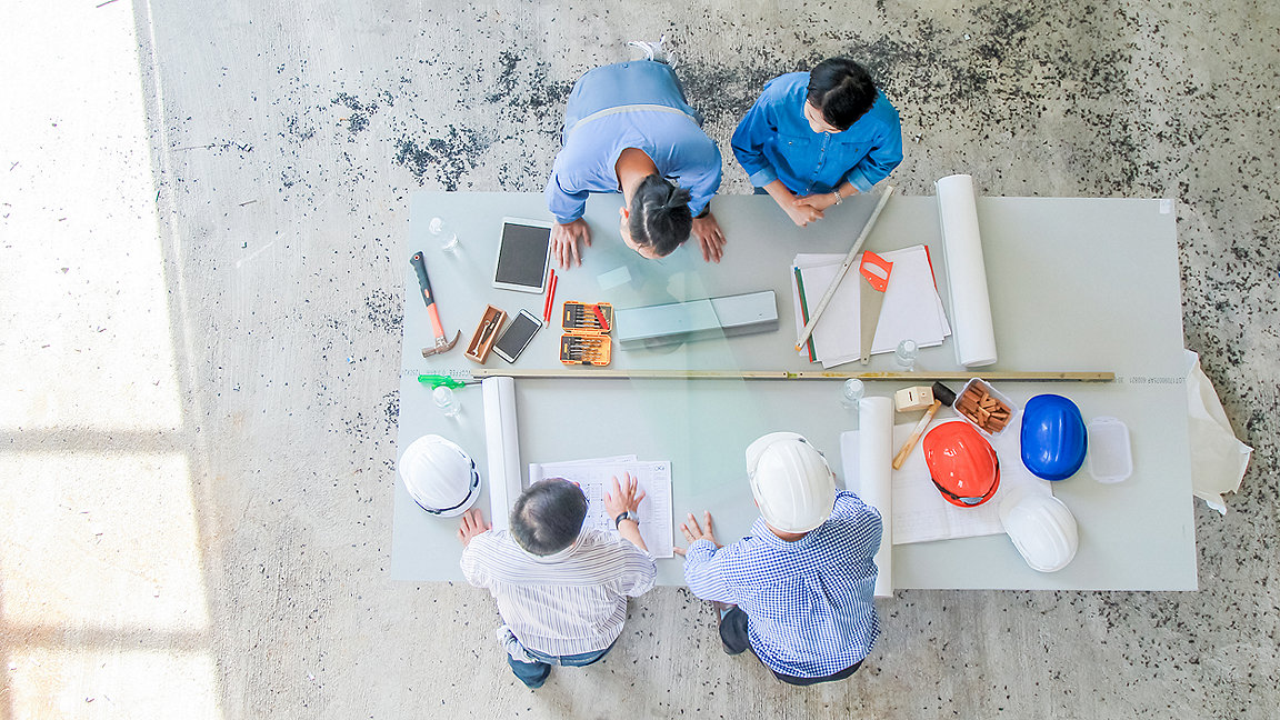 Overhead view of construction professionals discussing documents on a table in a building site