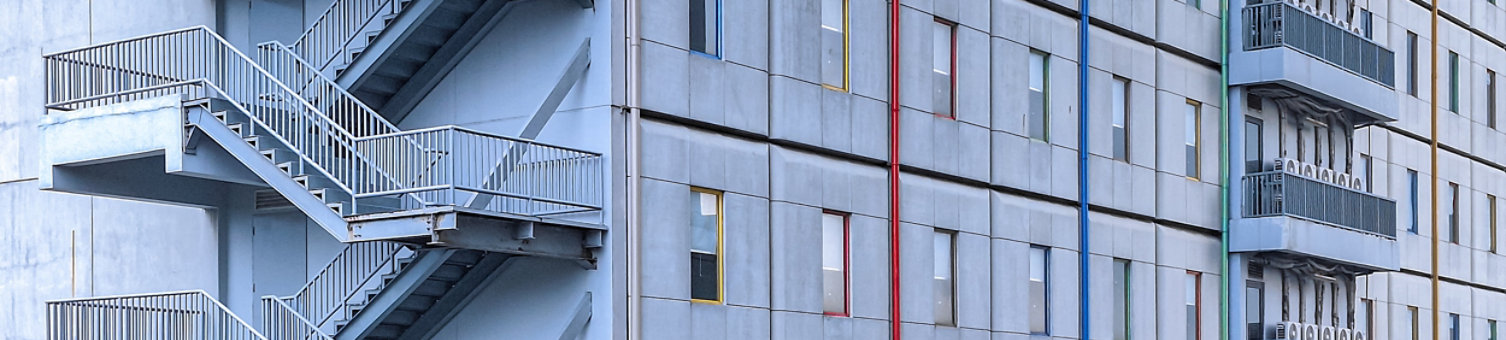Gray exterior of hotel building with colorful windows, exterior air conditioning and Fire escape stairs outside building.