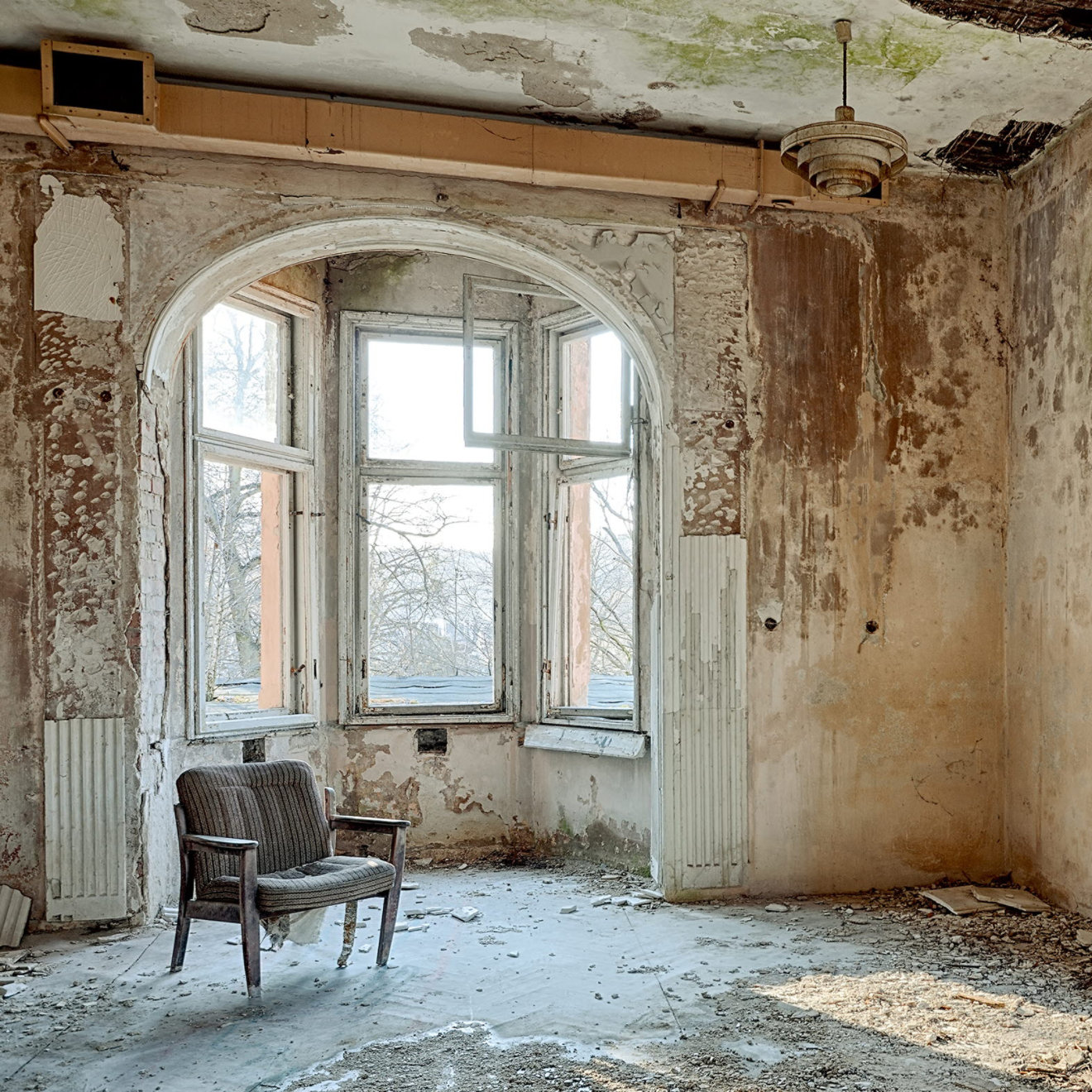 A dilapidated room with paint peeling off the walls and untreated wooden floorboards