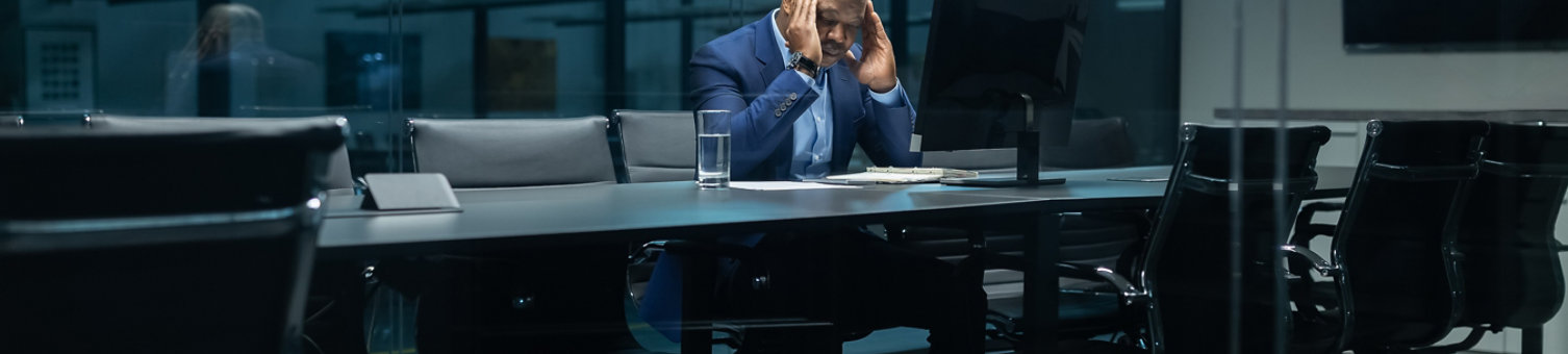 Stressed black businessman sitting alone in dark meeting room, holding his head