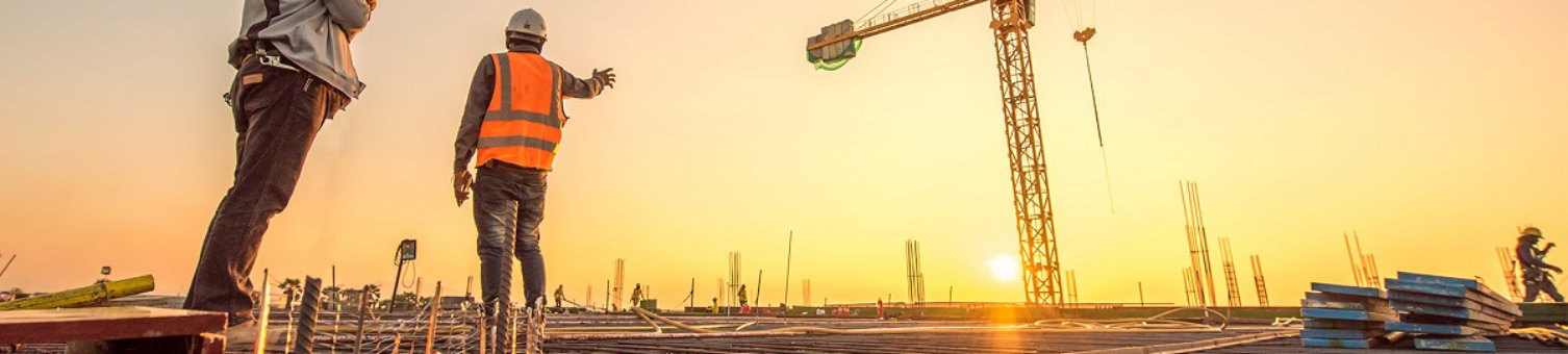 A man in a high-vis vest and white helmet looking up at a yellow crane