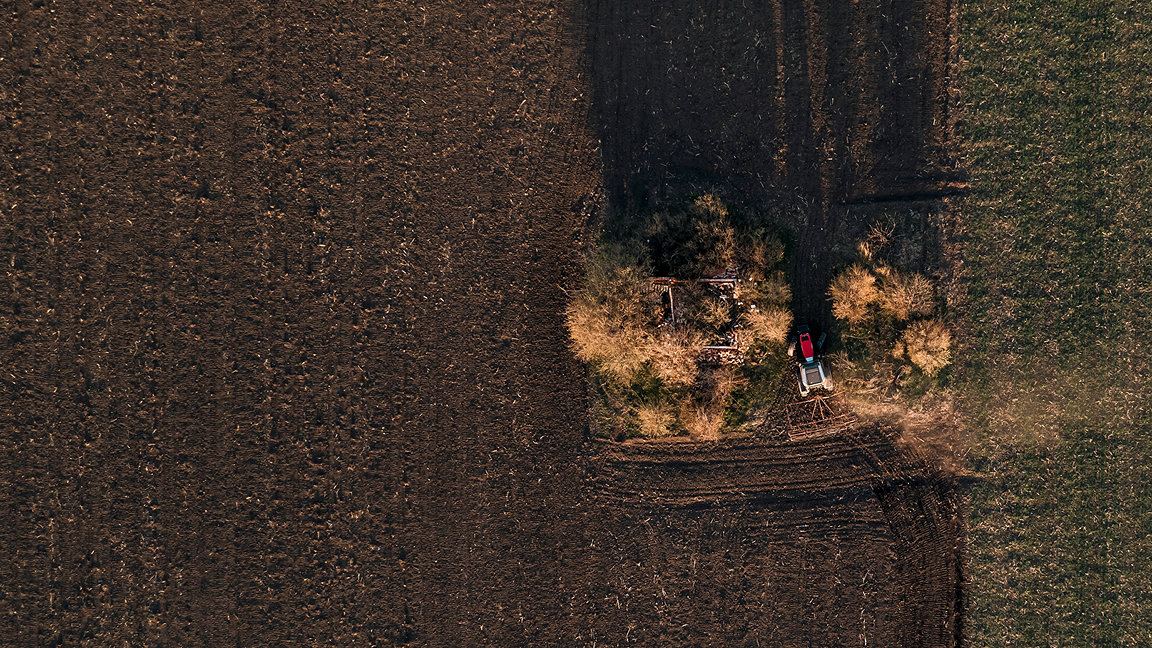 Aerial view of tractor with tiller attached performing soil tillage in field