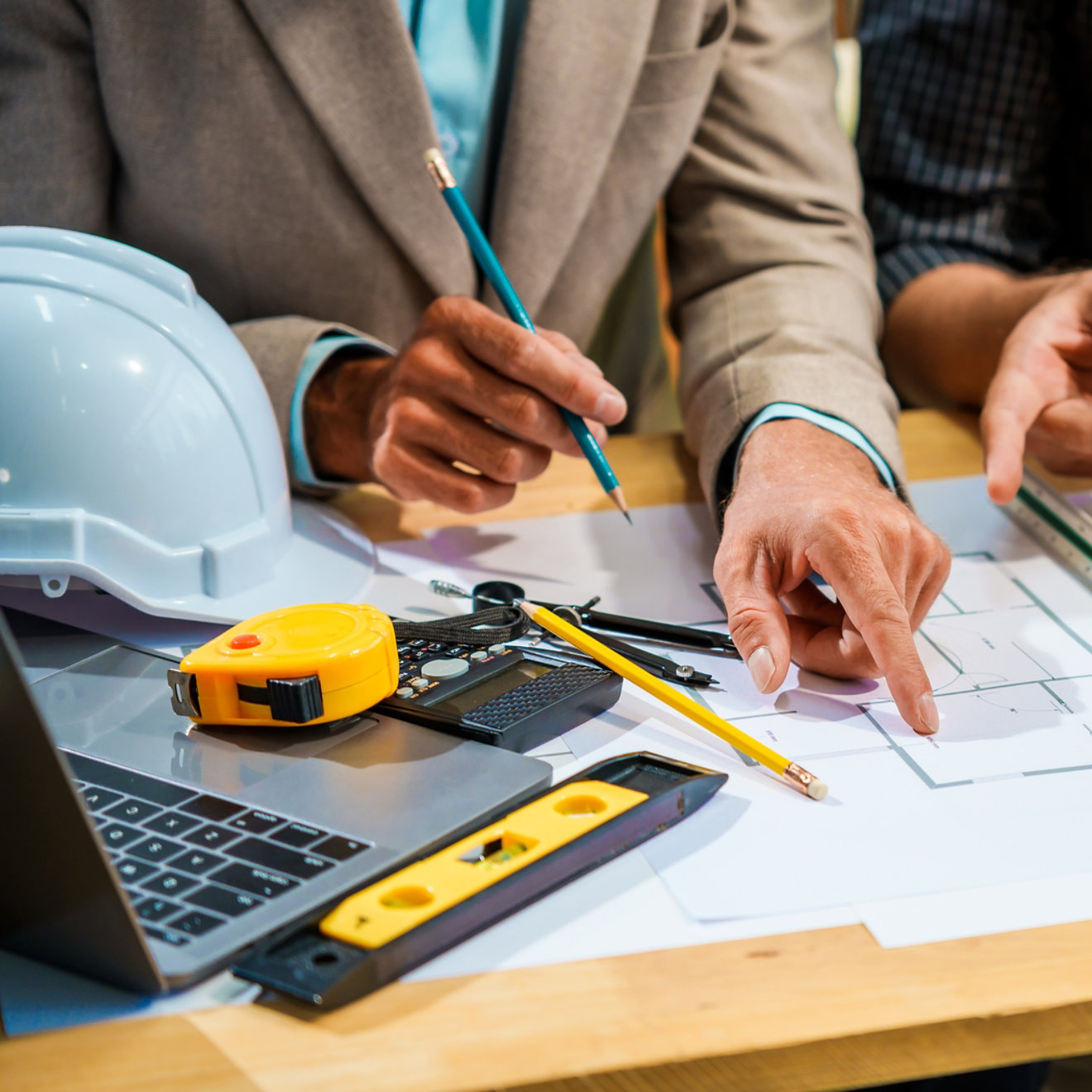 A Caucasian male engineer and an Italian male building contractor are planning and talking at a desk, examining house plans and a scale model with wooden textures for a renovation project.