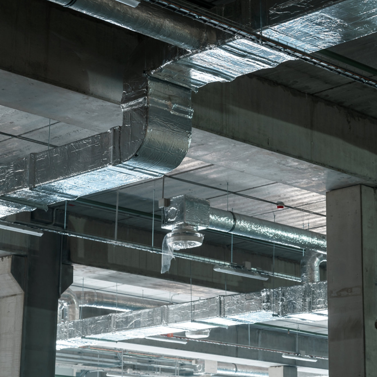 Air ventilation system on the ceiling in a large warehouse. Pipes made of silver insulating material hang from the ceiling inside the new building