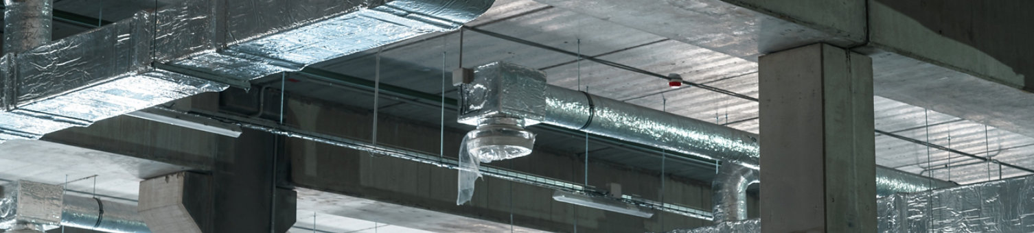 Air ventilation system on the ceiling in a large warehouse. Pipes made of silver insulating material hang from the ceiling inside the new building