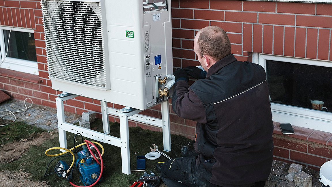 Man installing heat pump outside modern house