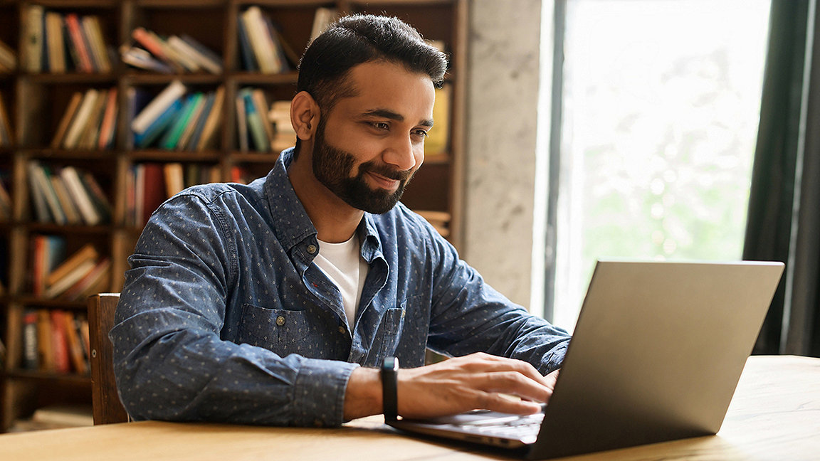Young Indian man in domestic setting, looking at laptop and smiling