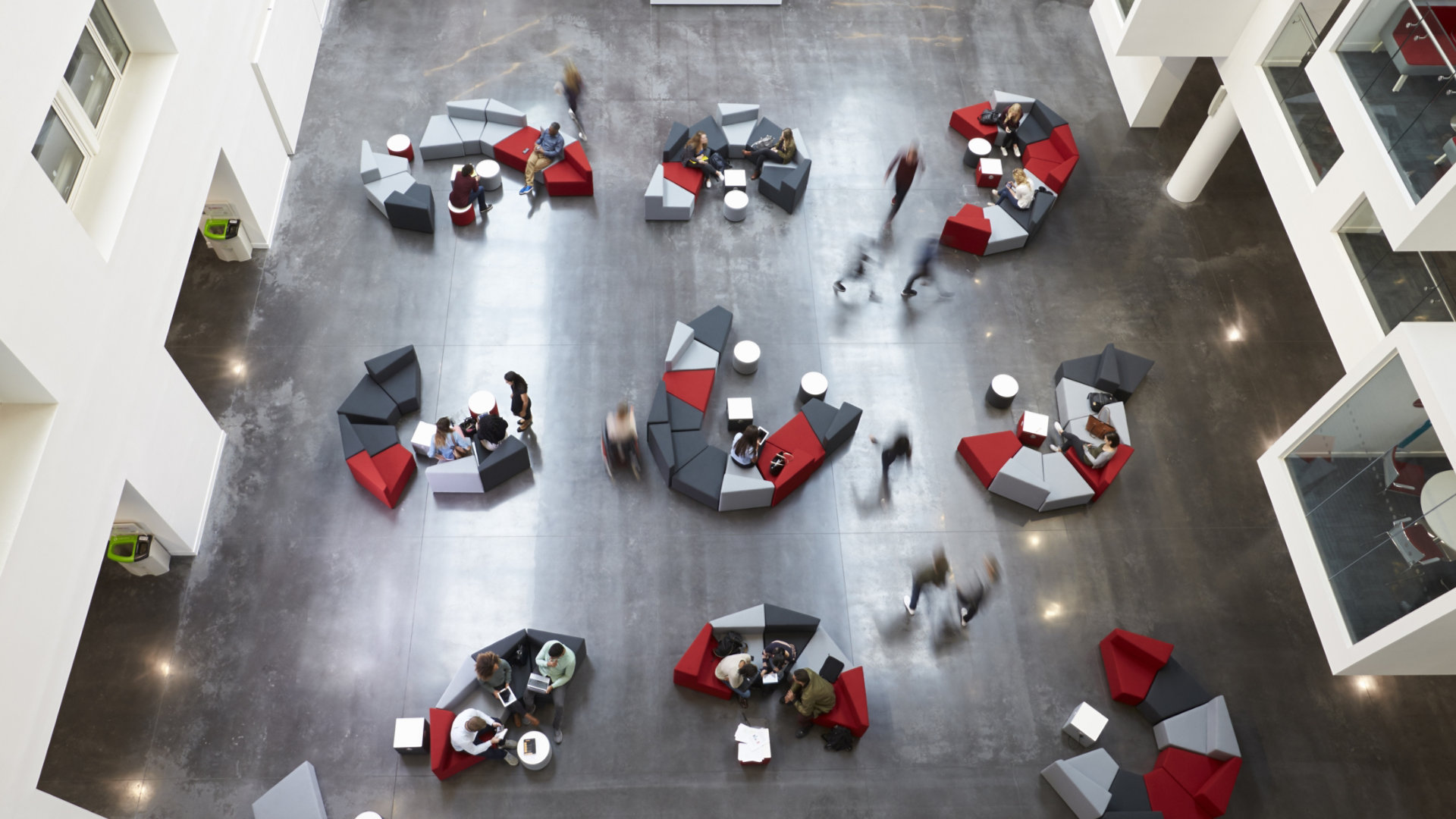 Long exposure photograph of groups of people on seating in a modern office environment viewed from above.