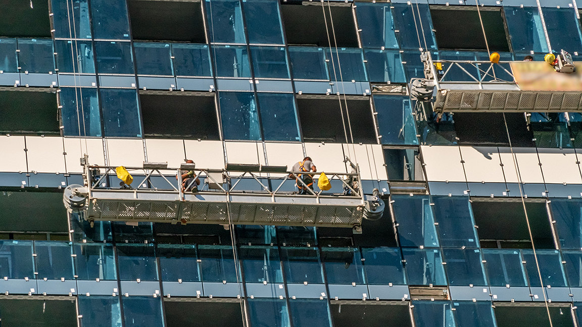 A group of workers in the cradle inspects the facade of a high-rise building. Glass building, inspection and maintenance of the facade. 