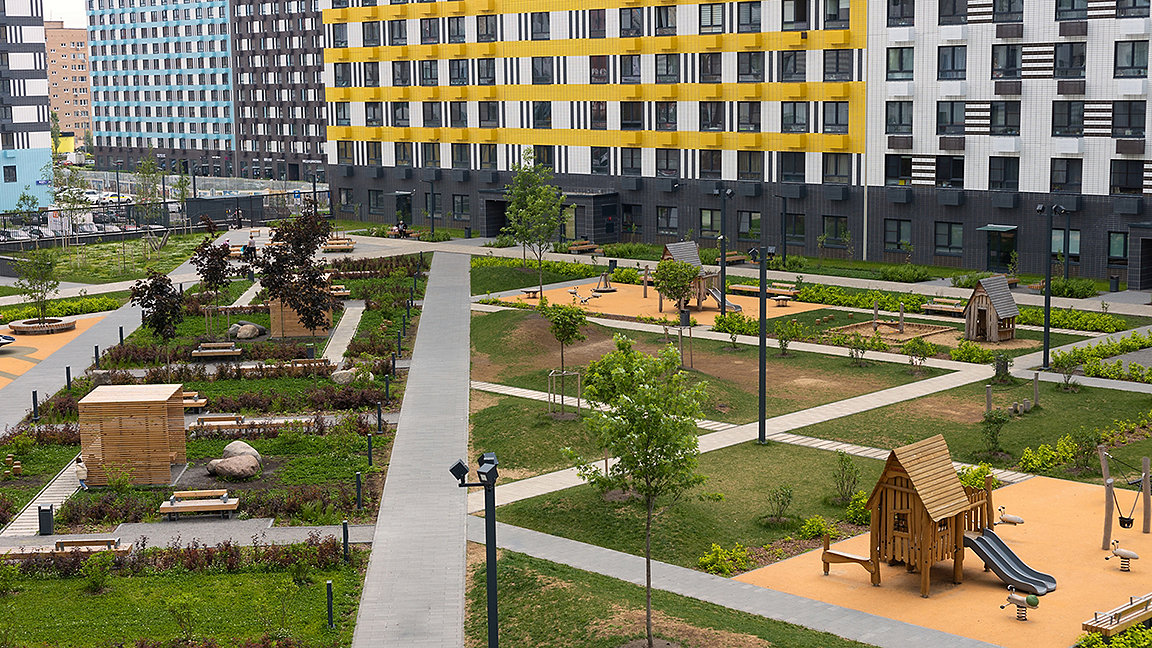Gardens with play equipment, grass spaces and seating areas in the middle of a development of new-build apartments