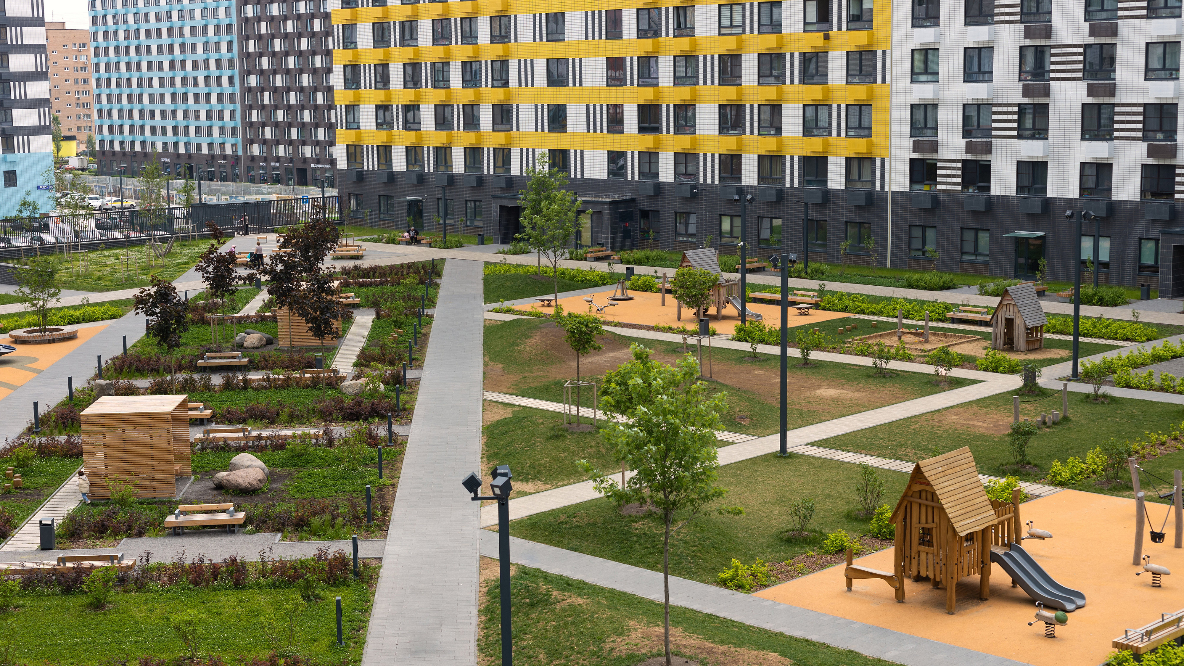 Gardens with play equipment, grass spaces and seating areas in the middle of a development of new-build apartments