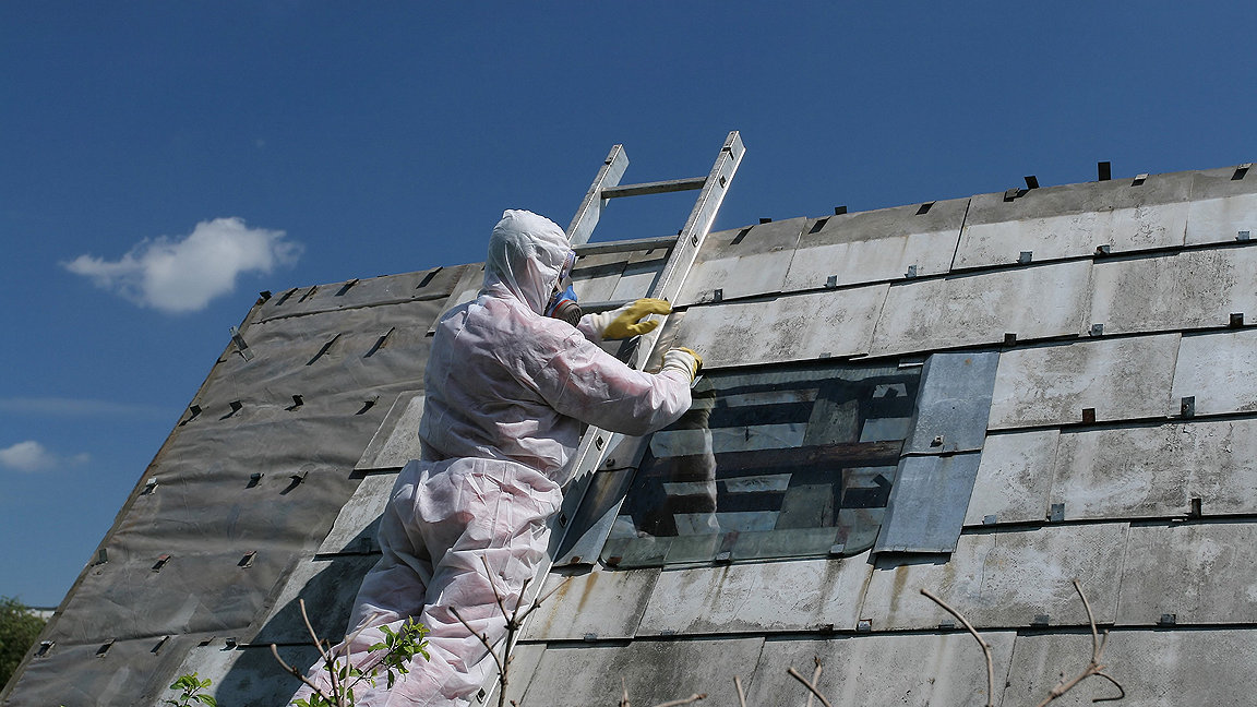Worker removing asbestos from building roof