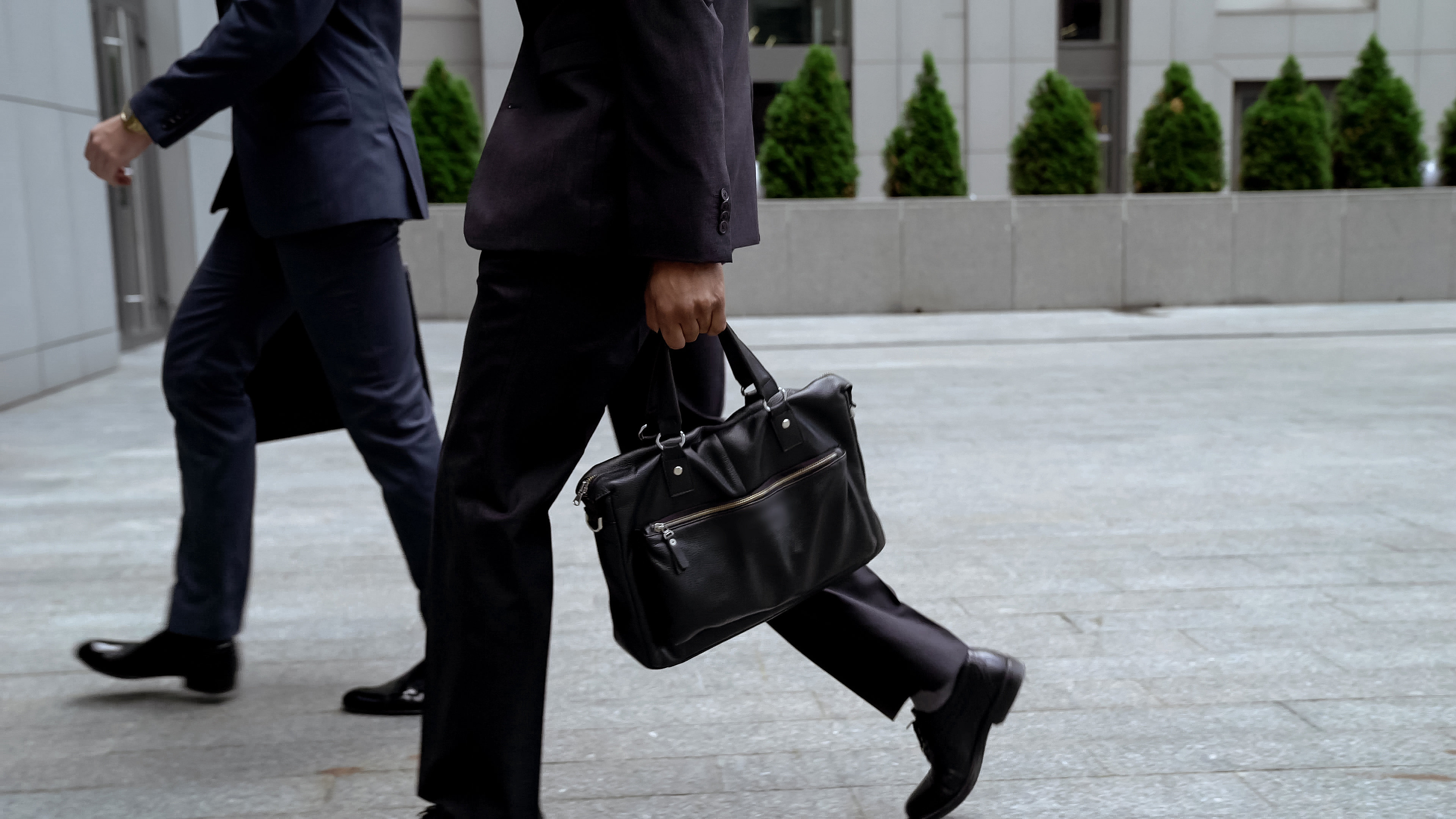 Two businessmen in dark suits, faces to visible, walking towards an office