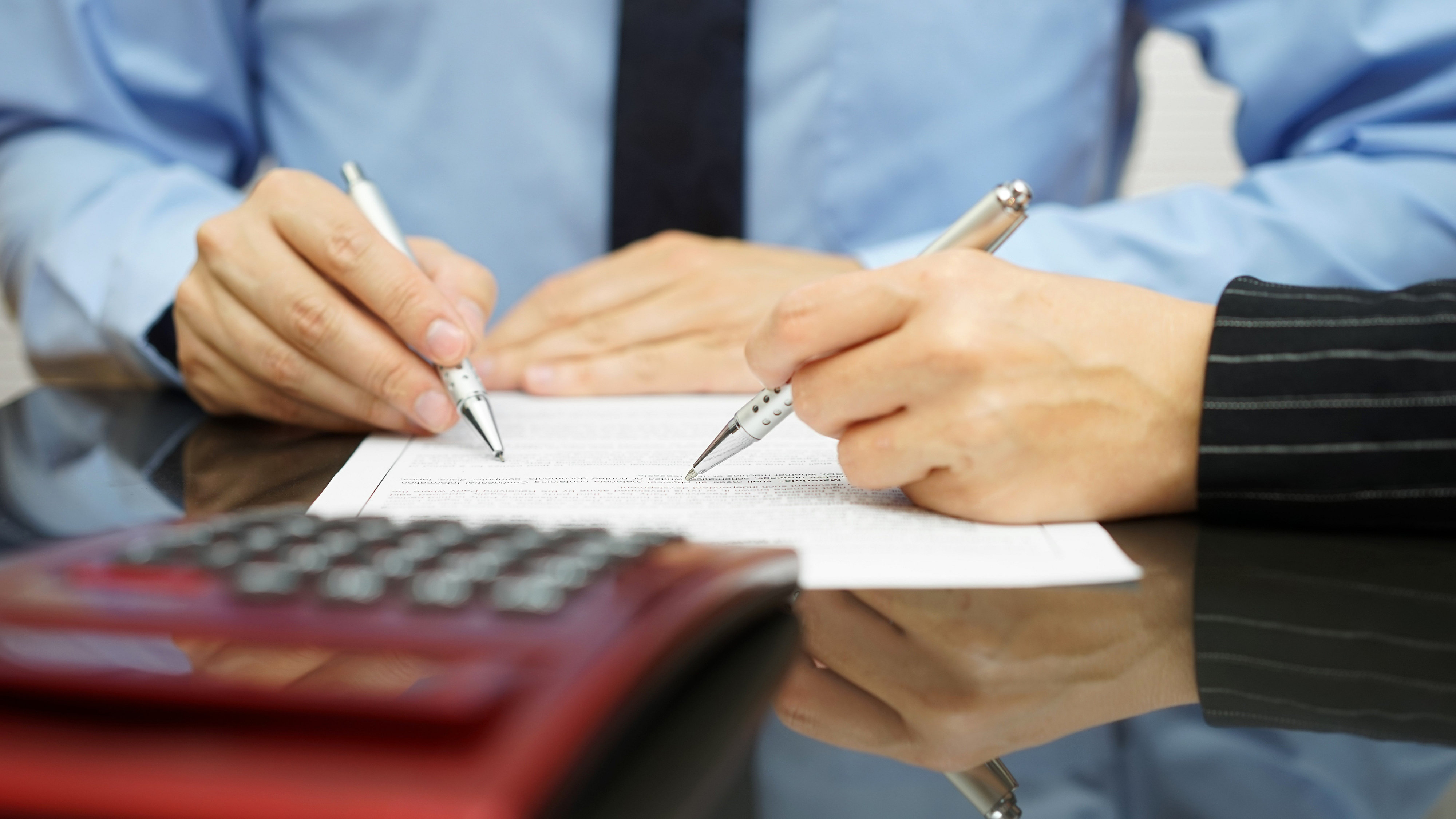 Businessman and businesswoman signing a document, seated at a desk