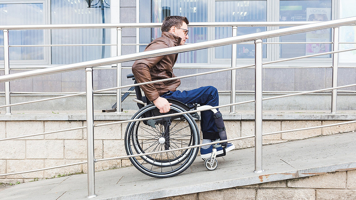 Photo of a man in a wheelchair using a ramp to enter a building.