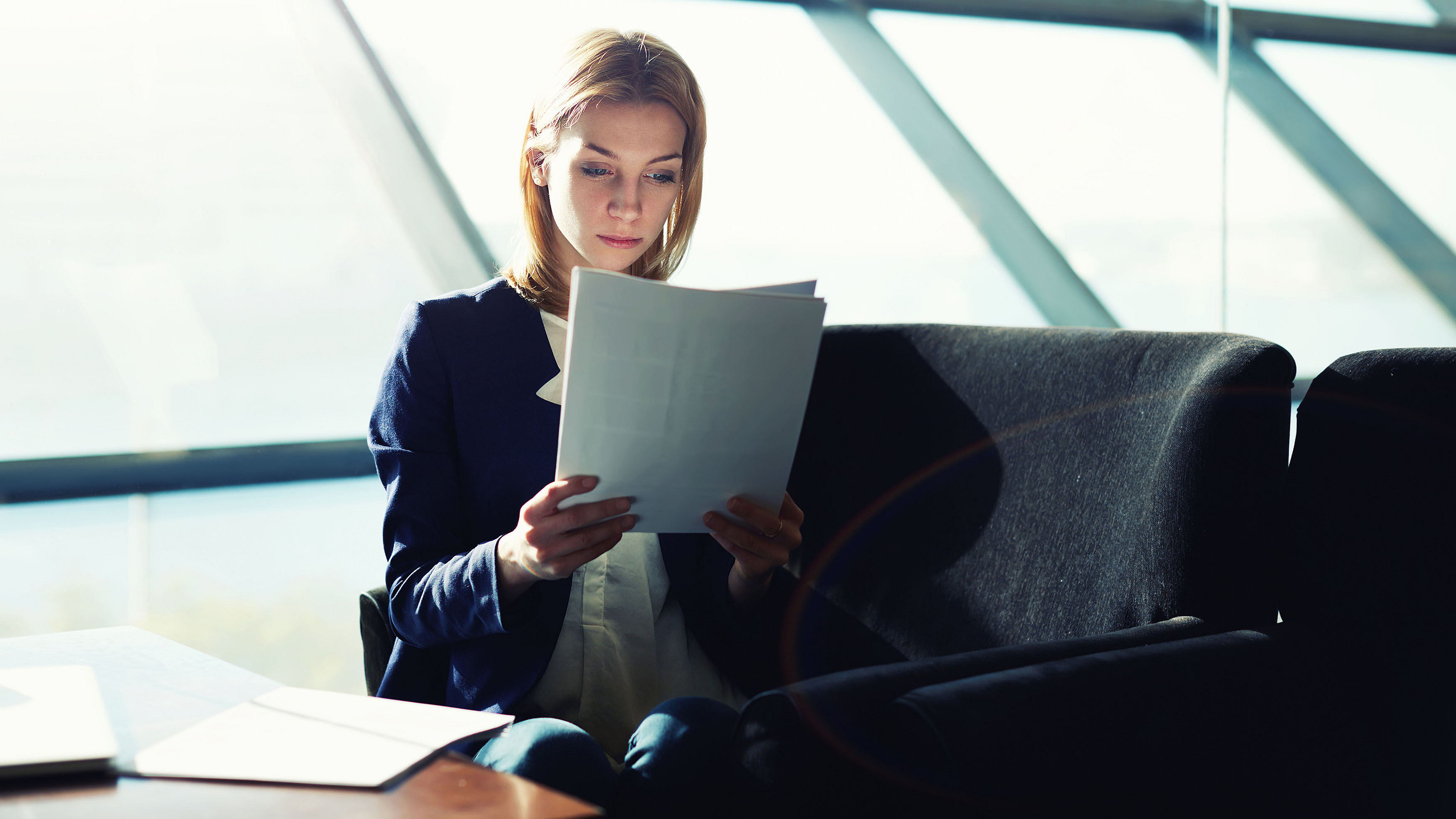 Young female professional reading paperwork in front of brightly lit windows