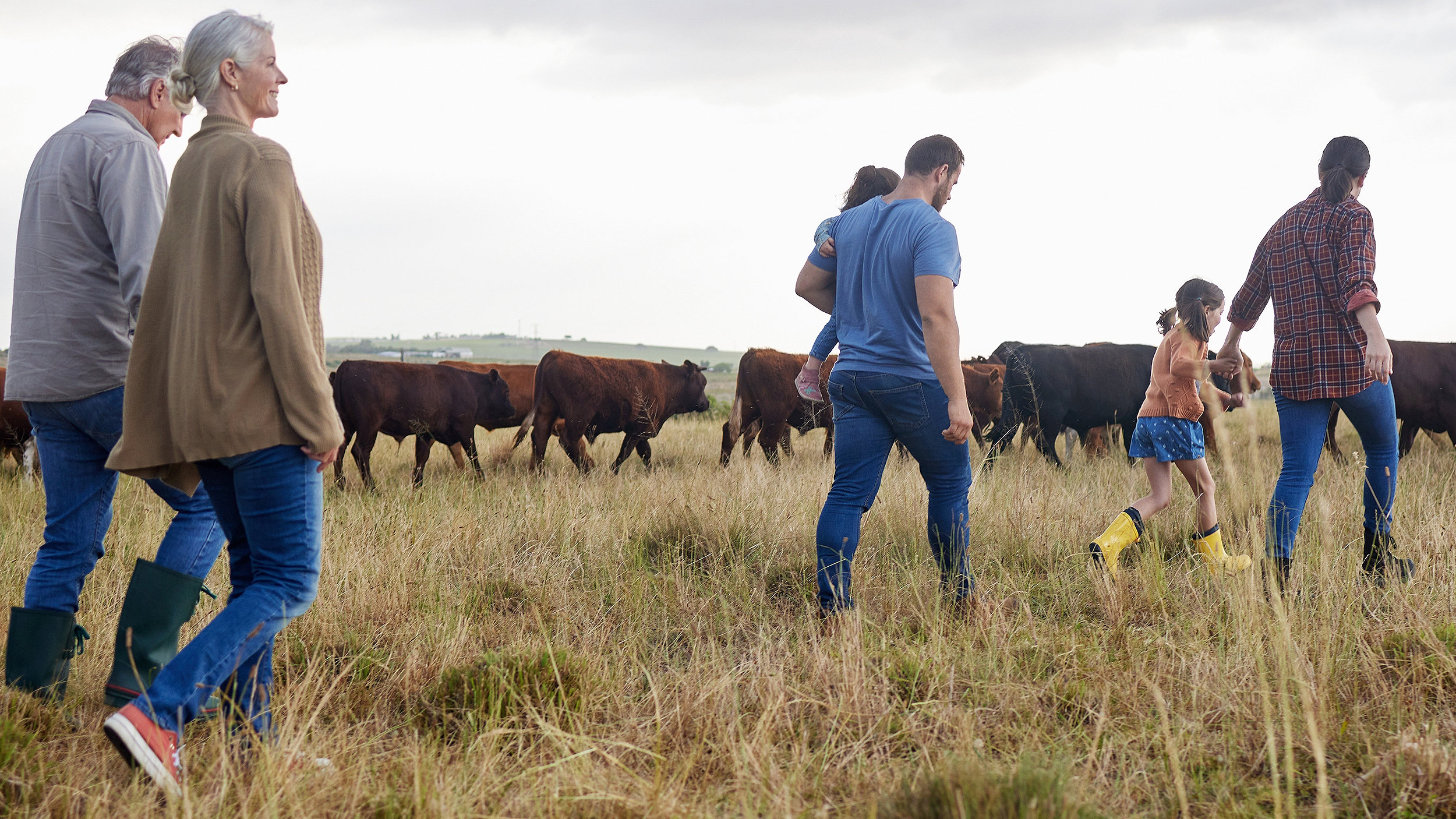 Family of farmers walking through field of cattle, three generations