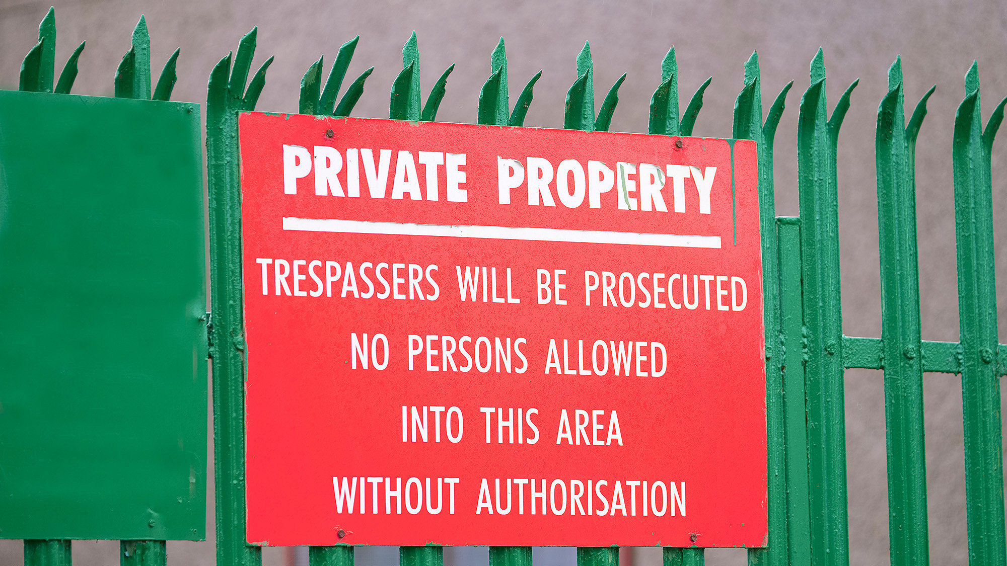 Photo of a red sign on a green fence with the words 'trespassers will be prosecuted'