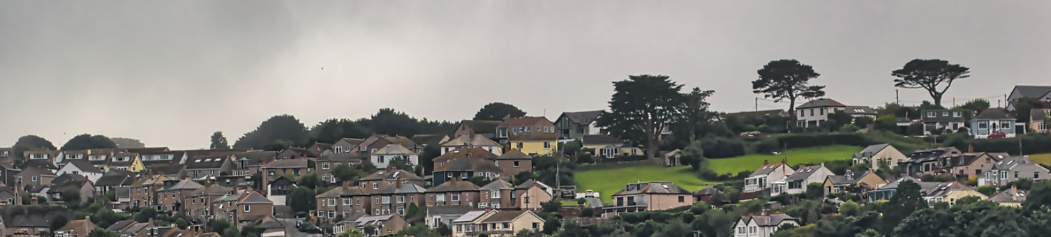 A scenic view of a hillside town with densely packed houses, showcasing a mix of architectural styles. In Penzance, Cornwall, UK.