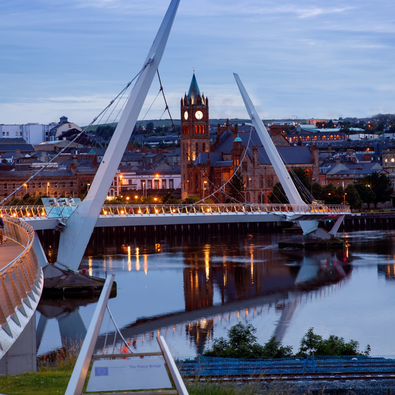 Derry, Ireland. Illuminated Peace bridge in Derry Londonderry, City of Culture, in Northern Ireland with city center at the background. Night cloudy sky with reflection in the river at the dusk