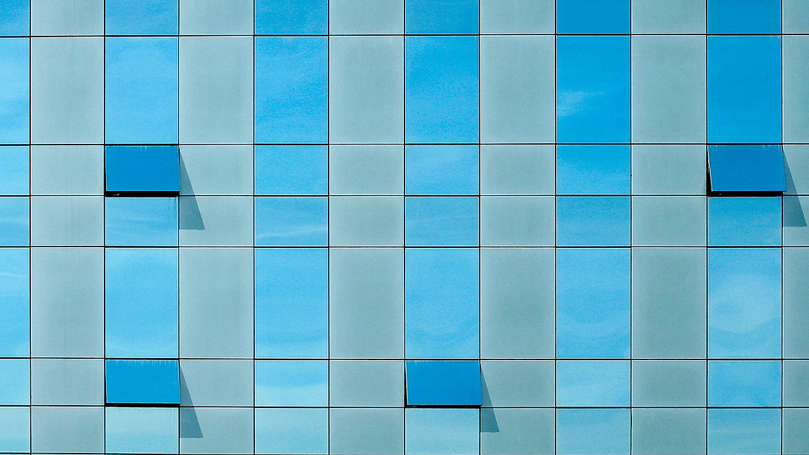 Facade of glass-fronted office building on bright day, with three windows hinged open
