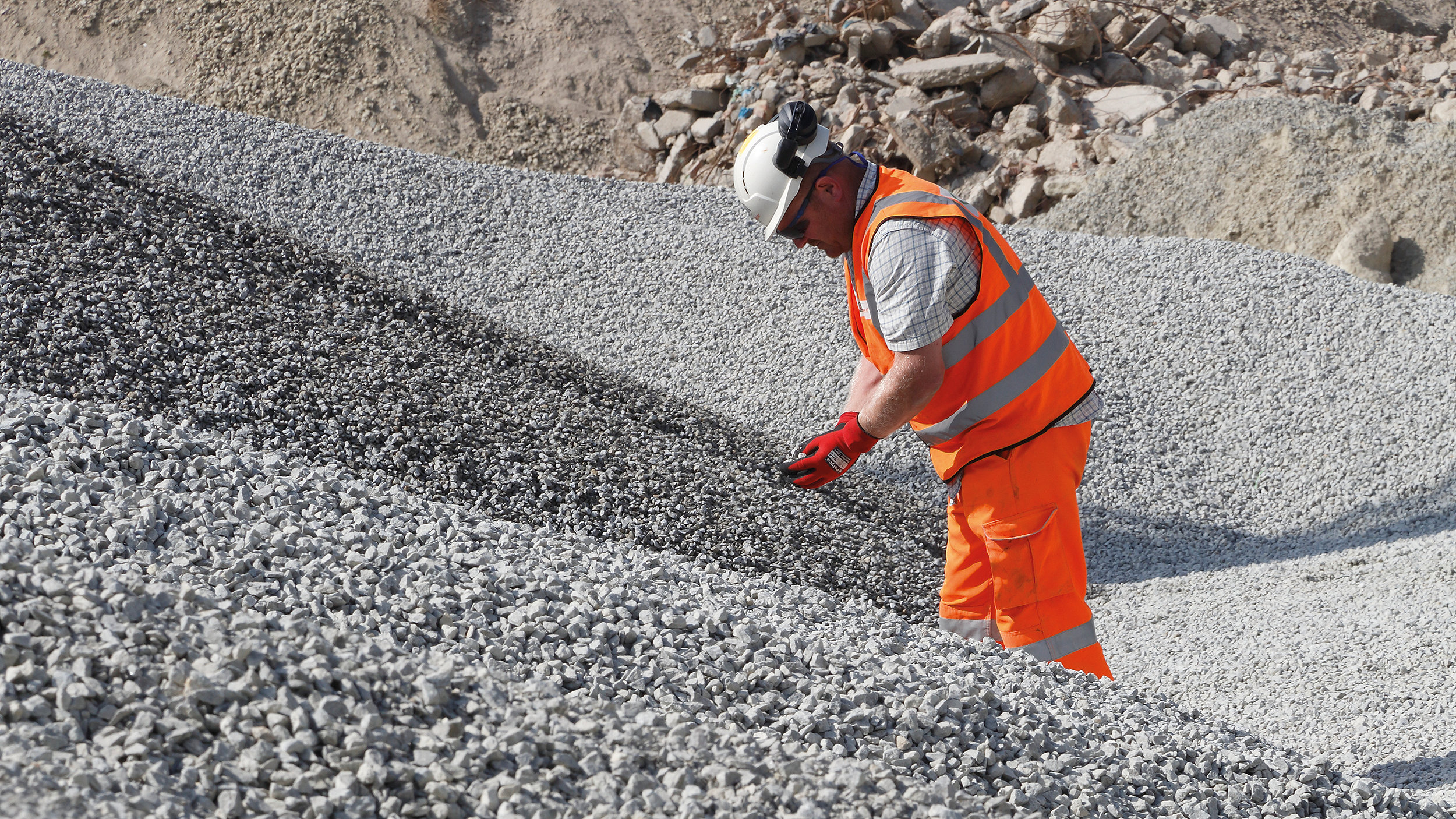 Male worker in high vis, gloves and hard hat in middle of aggregate pile