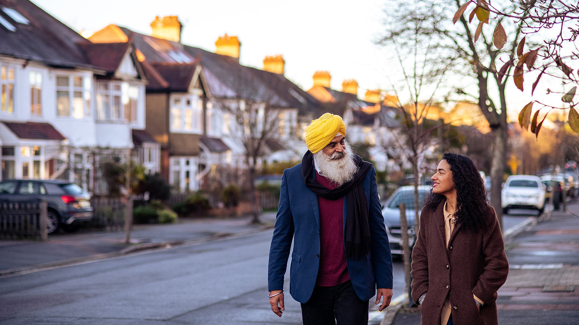 Photo of older Sikh man and younger woman walking past residential properties