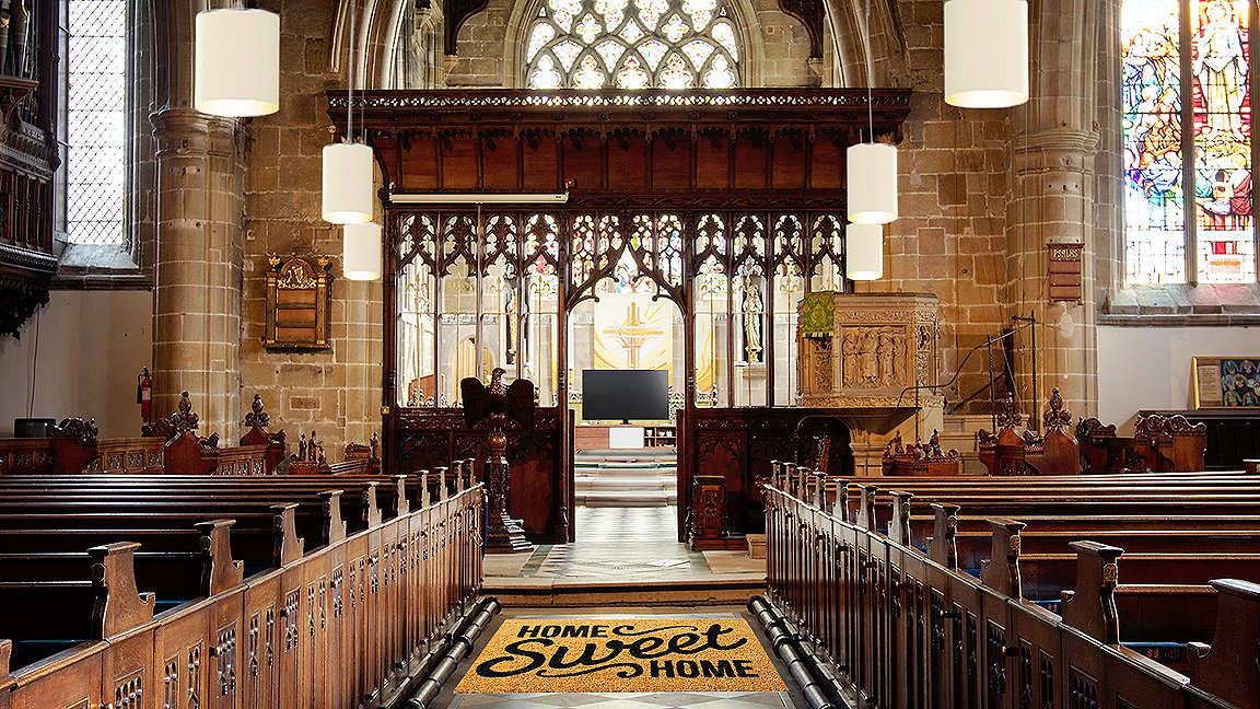 Looking down the aisle of a church with a mat in foreground saying ' home sweet home' and a TV replacing the pulpit