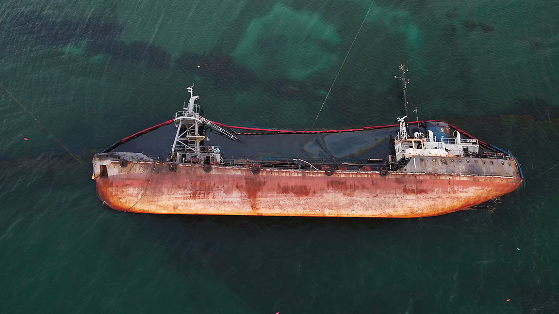 Top view of an old tanker, overturned in the sea, with oil spilling from it