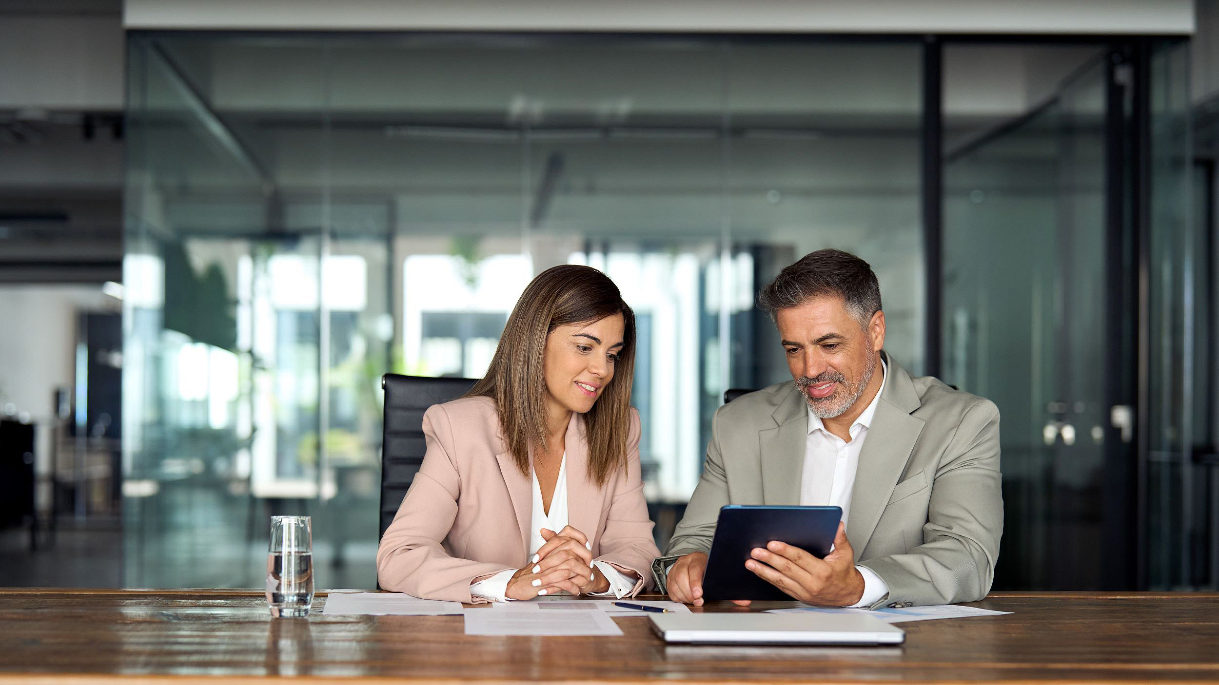 Professional business executives office team working using digital tablet computer sitting at table. Two middle aged colleagues company board discussing smart technology at corporate meeting.