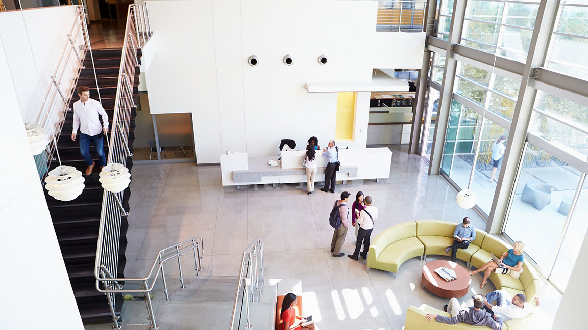 Modern office reception viewed from above with people at reception desk, sitting on sofas and standing just outside