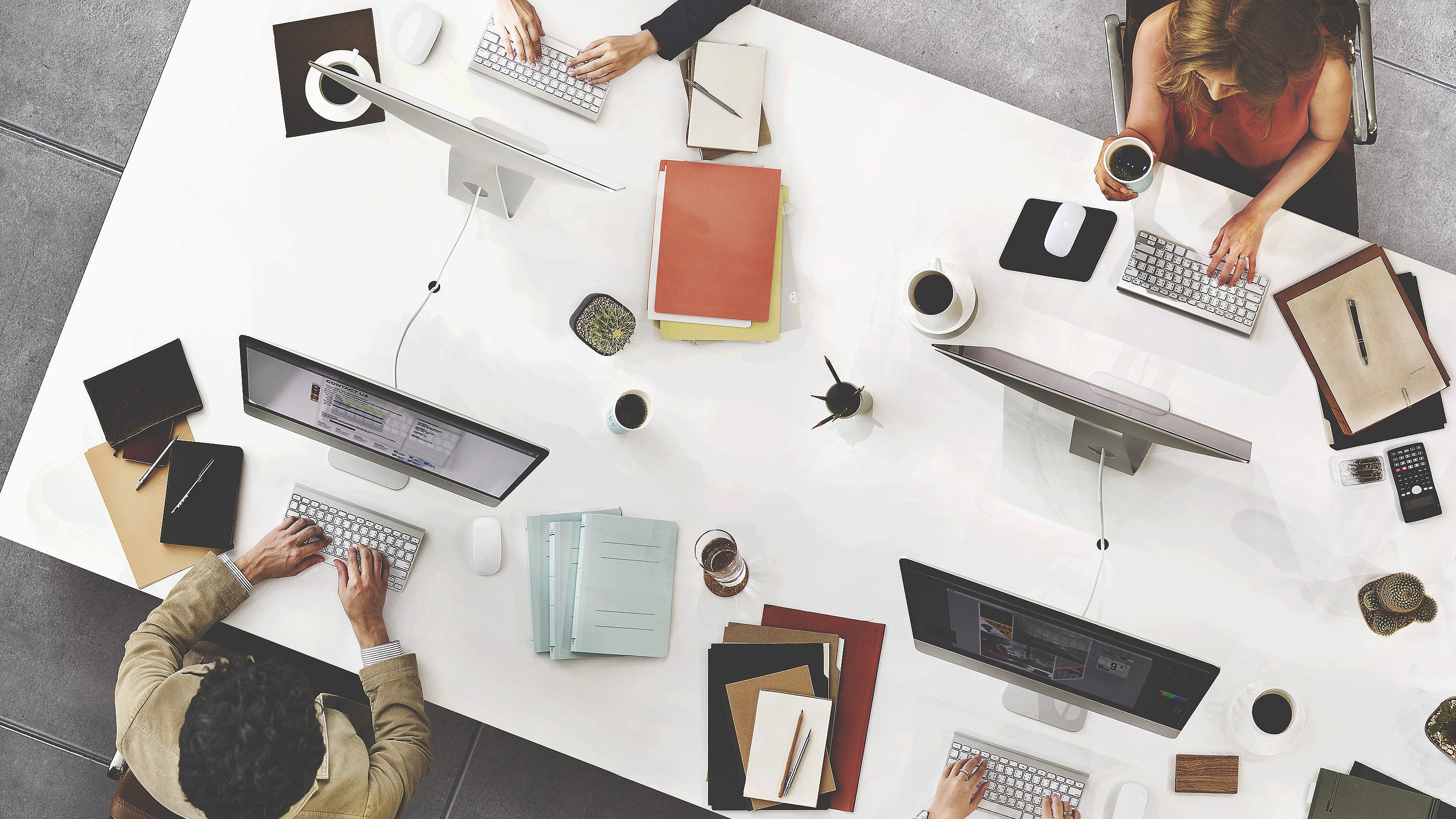 Overhead picture of shared desk with people working across from each other - computers and paper files on the desk