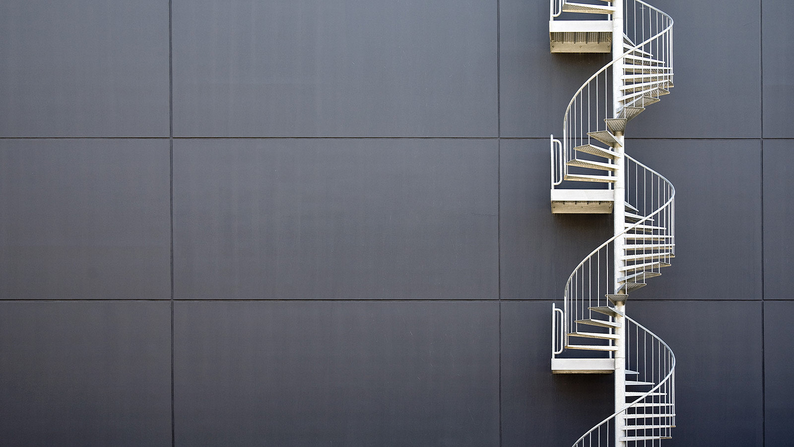 White fire escape running down the side of a grey cladded building.