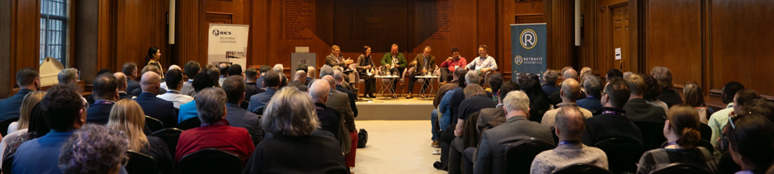 A view of the Quality in Retrofit Summit taken from the back of the room showing the attendees, and the panel on stage