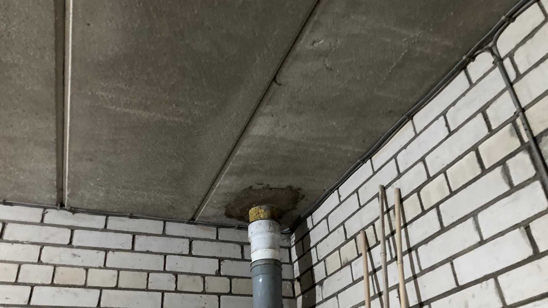 A photograph of three RAAC panels forming the corner of a ceiling in a domestic garage. One of the panels has been cut to accommodate a drainage pipe