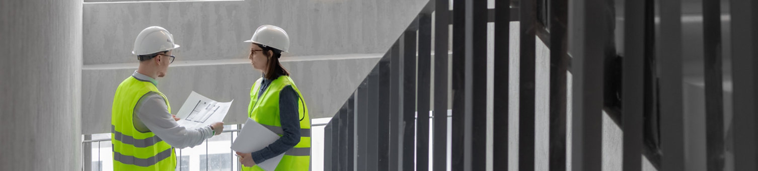 two engineers, a man and a woman in white helmets and green protective vests, work at the construction site, professional and licensed engineers in construction and fire safety technology take