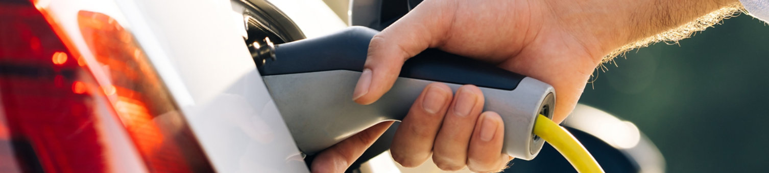 The driver of the electric car inserts the electrical connector to charge the batteries. Unrecognizable man attaching power cable to electric car. Electric vehicle Recharging battery charging port.
