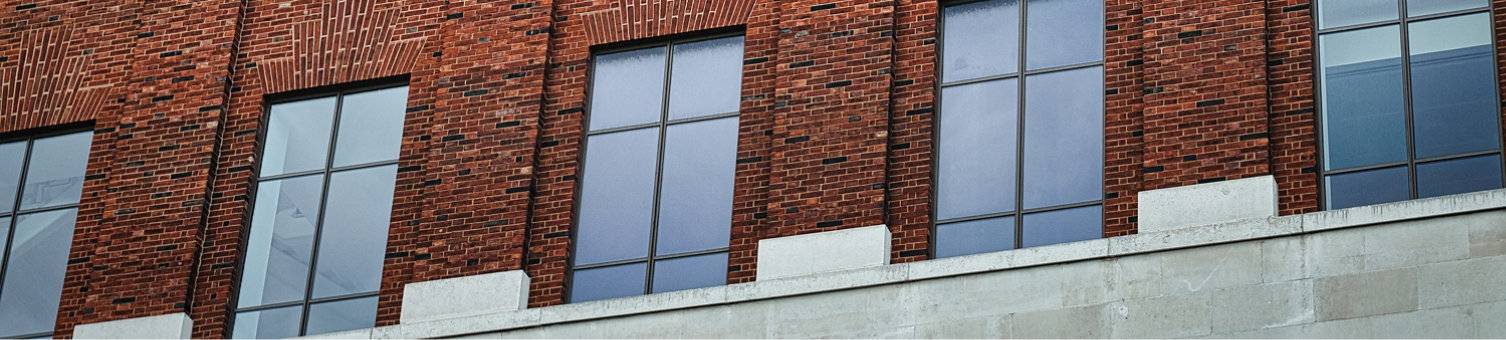 Facade of a brick building with symmetrical windows reflecting the sky, architectural background in Leeds, UK.