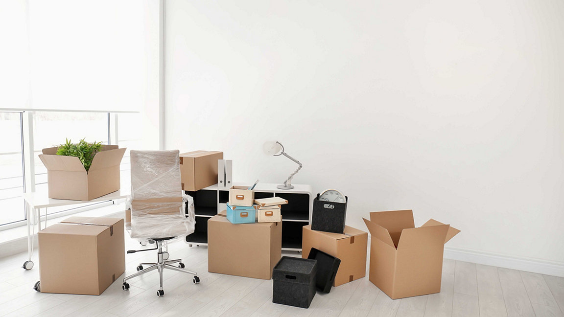 Desks, chairs and folders packed up for an office move in brightly lit modern office space