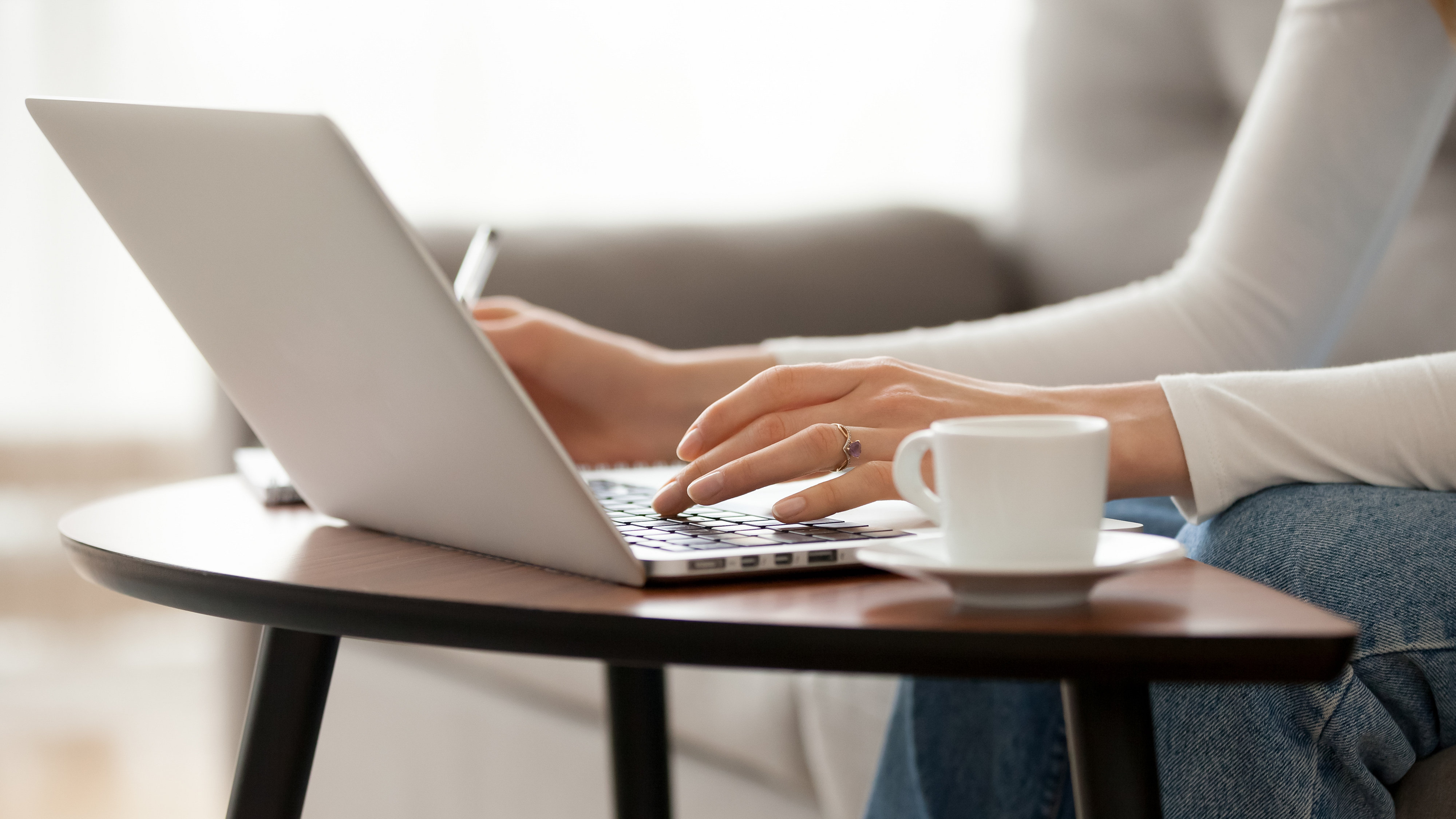 Close up of woman's hands typing on a laptop on coffee table