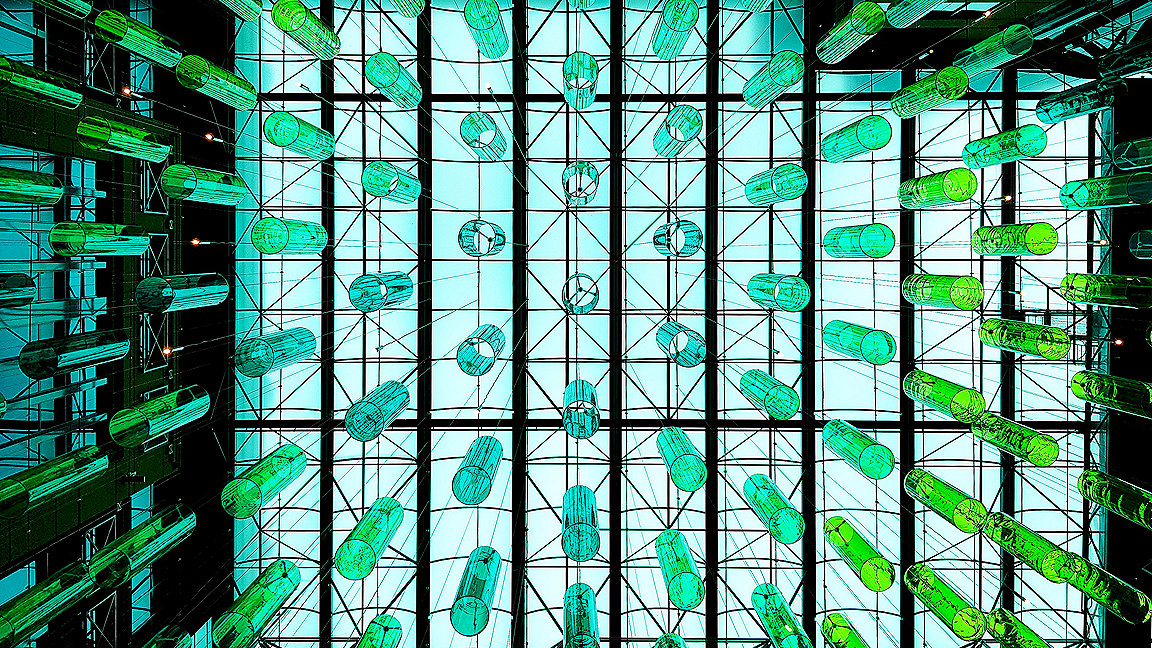 Looking up at green glass cylinders hanging from the glass ceiling